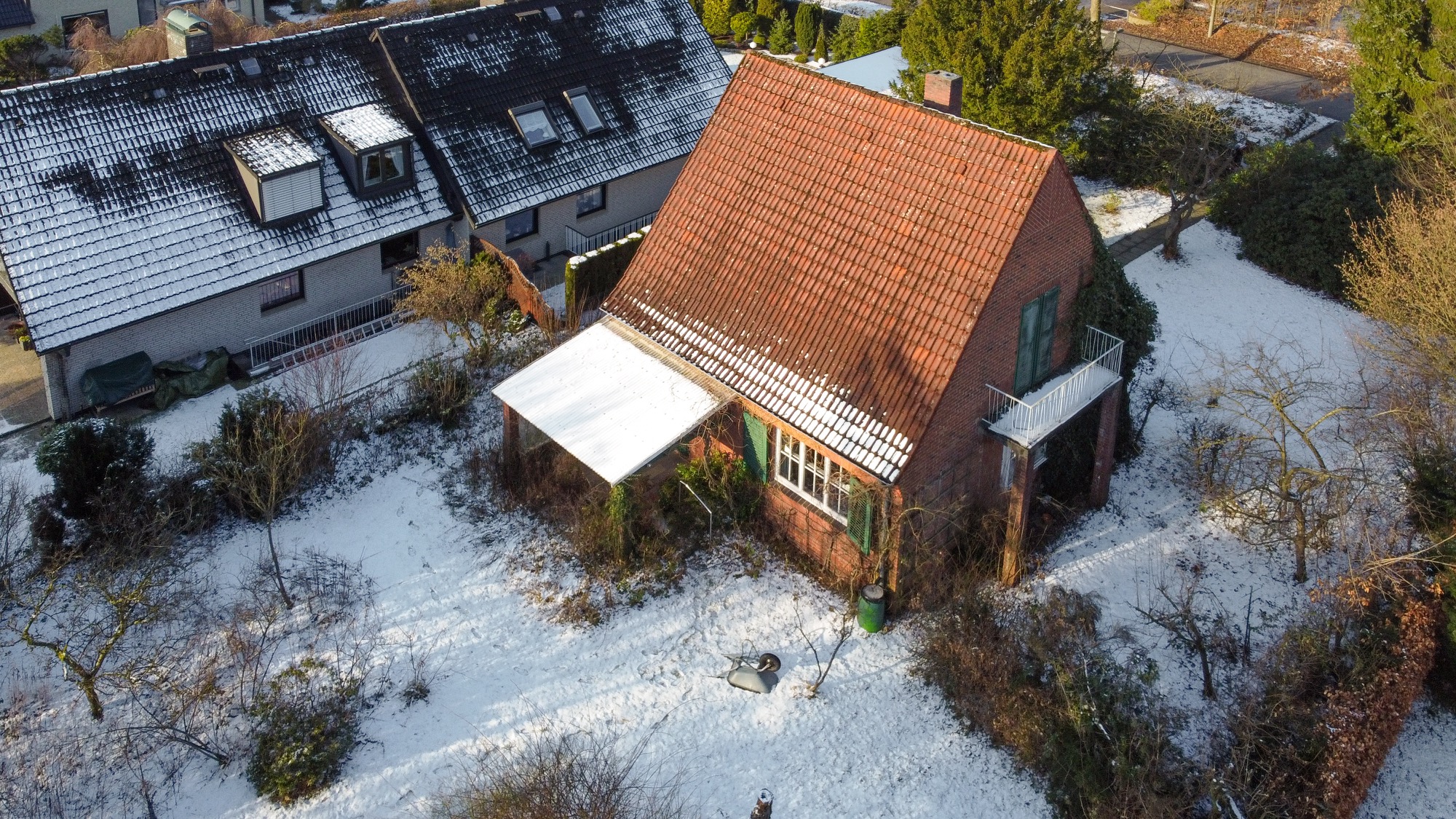 Einfamilienhaus mit rotem Dach und schneebedecktem Garten, umgeben von Bäumen.